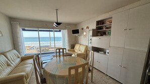 Una sala de estar con vista a la playa, una mesa de comedor y una kitchenette.