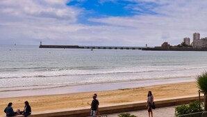 Una playa con un paseo marítimo, un faro y edificios al fondo.