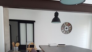 Ett modernt matområde med ett långt bord, två lila stolar, en svart hänglampa, en väggklocka och en liten träpall.