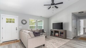 Ein Wohnzimmer mit einem beigefarbenen Sofa, einem Fernseher und einem Deckenventilator.