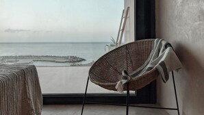 A room with a large window overlooking a beach, a wicker chair, and a ladder leaning against the wall.