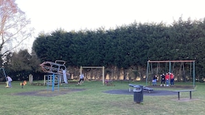 A park with playground equipment, a bench, and a trash bin. - 3 Bed Broomfield Road Newport Shropshire (Newport)