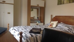 A bedroom with a bed, a wooden wardrobe, a nightstand with a mirror, and a painting on the wall. - 3 Bed Broomfield Road Newport Shropshire (Newport)