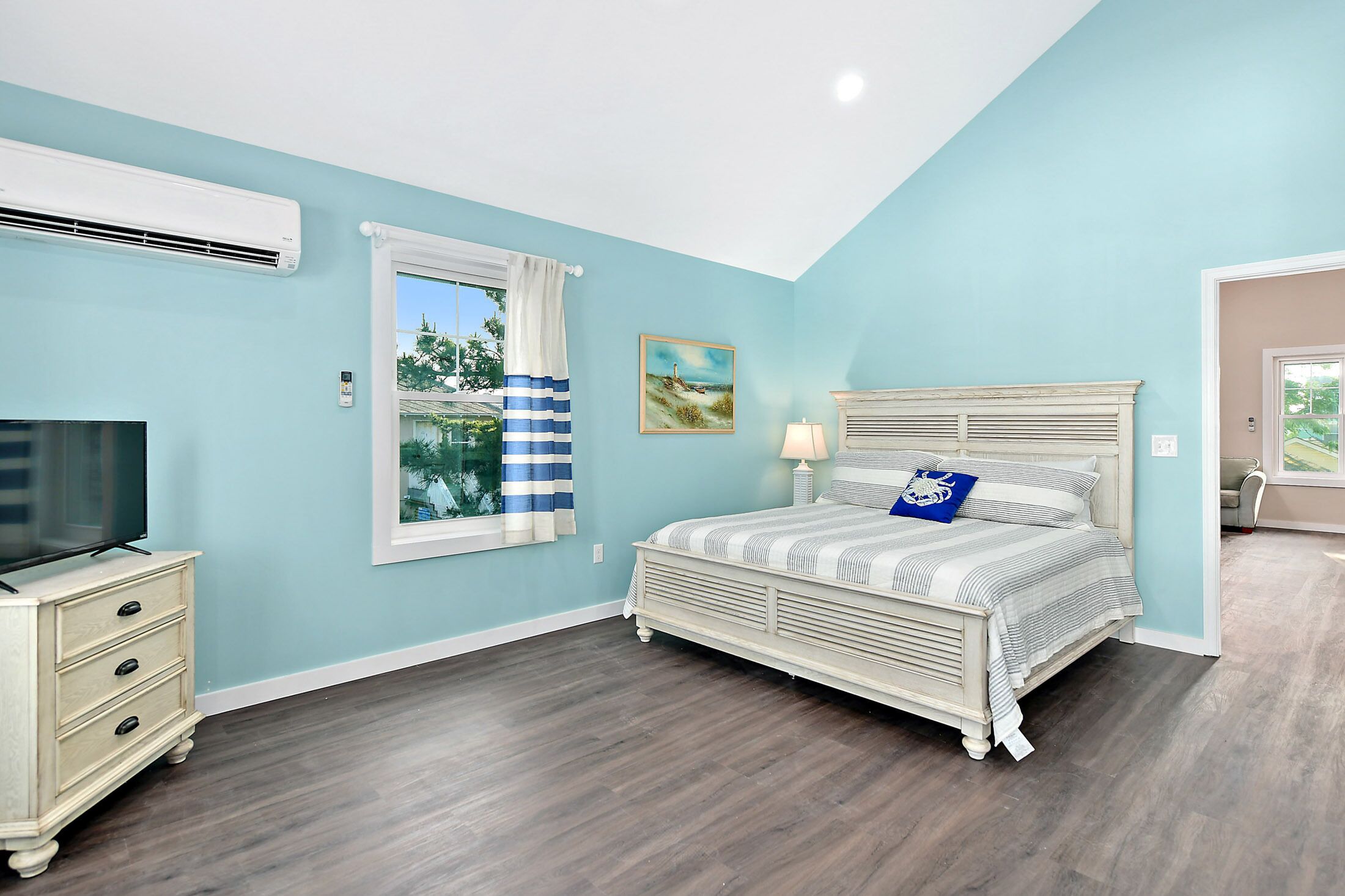 A bedroom with a bed, a TV, a dresser, and a window with curtains.