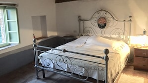 Een eenpersoonsbed met een metalen frame en een decoratief hoofdeinde, een nachtkastje met een lamp, en een raam met uitzicht.
