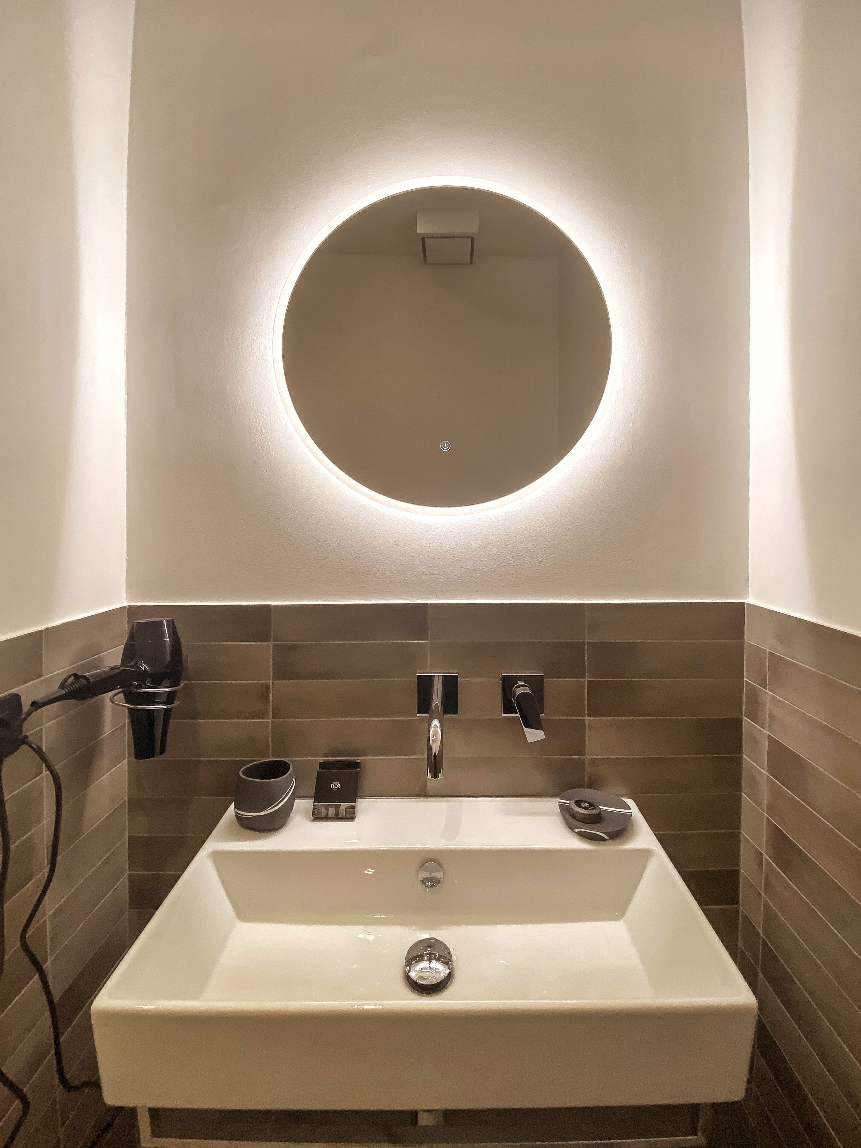 A bathroom with a white sink, a round mirror, a hairdryer, and a towel rack.