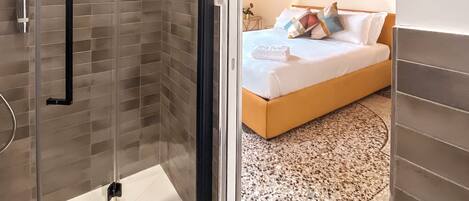 Un baño moderno con ducha de vidrio y un dormitorio con cama, mesita de noche y un adorno en la pared.