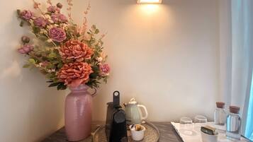 Una lámpara de pared, un florero con flores, una cafetera y una bandeja con tazas y una botella de agua.