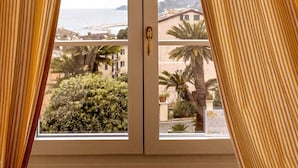 A window with yellow curtains, a view of a coastal area with buildings and palm trees.