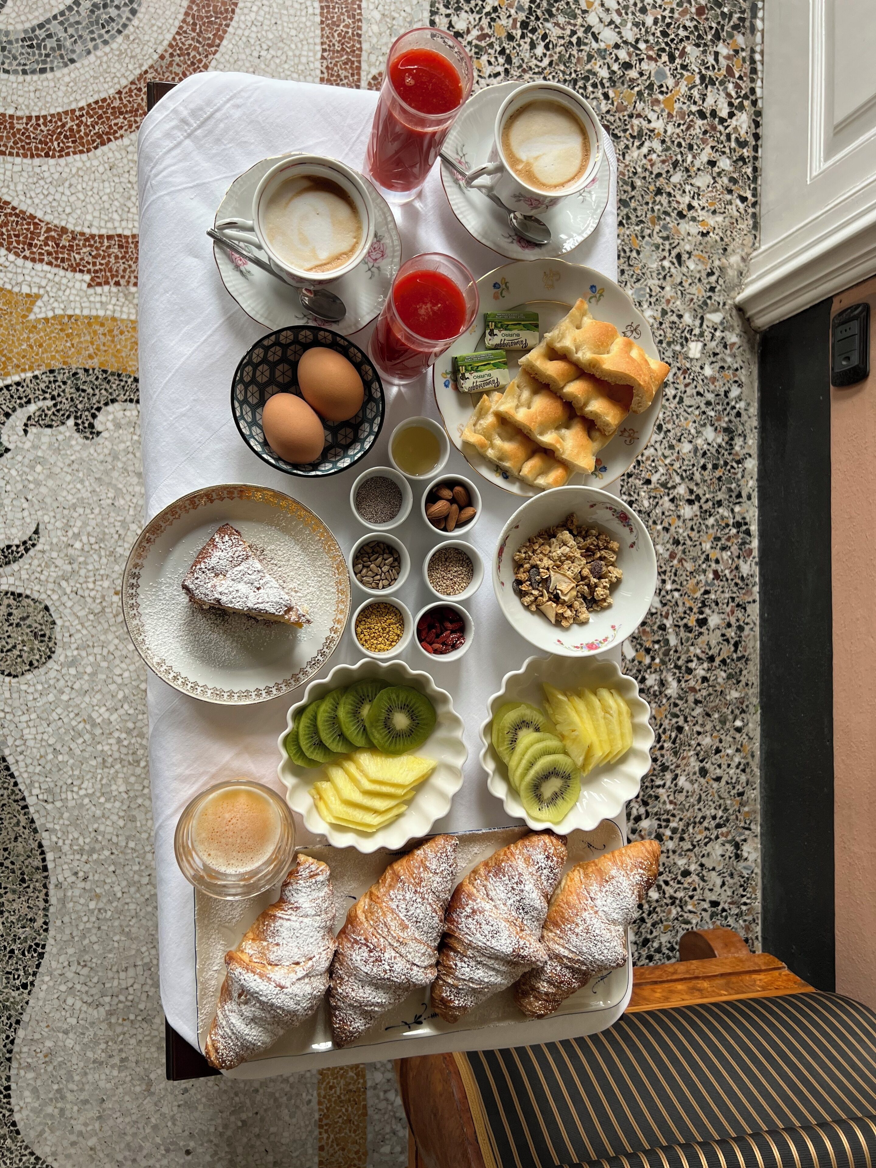 A breakfast tray with various foods and drinks, including eggs, bread, pastries, and a glass of juice.