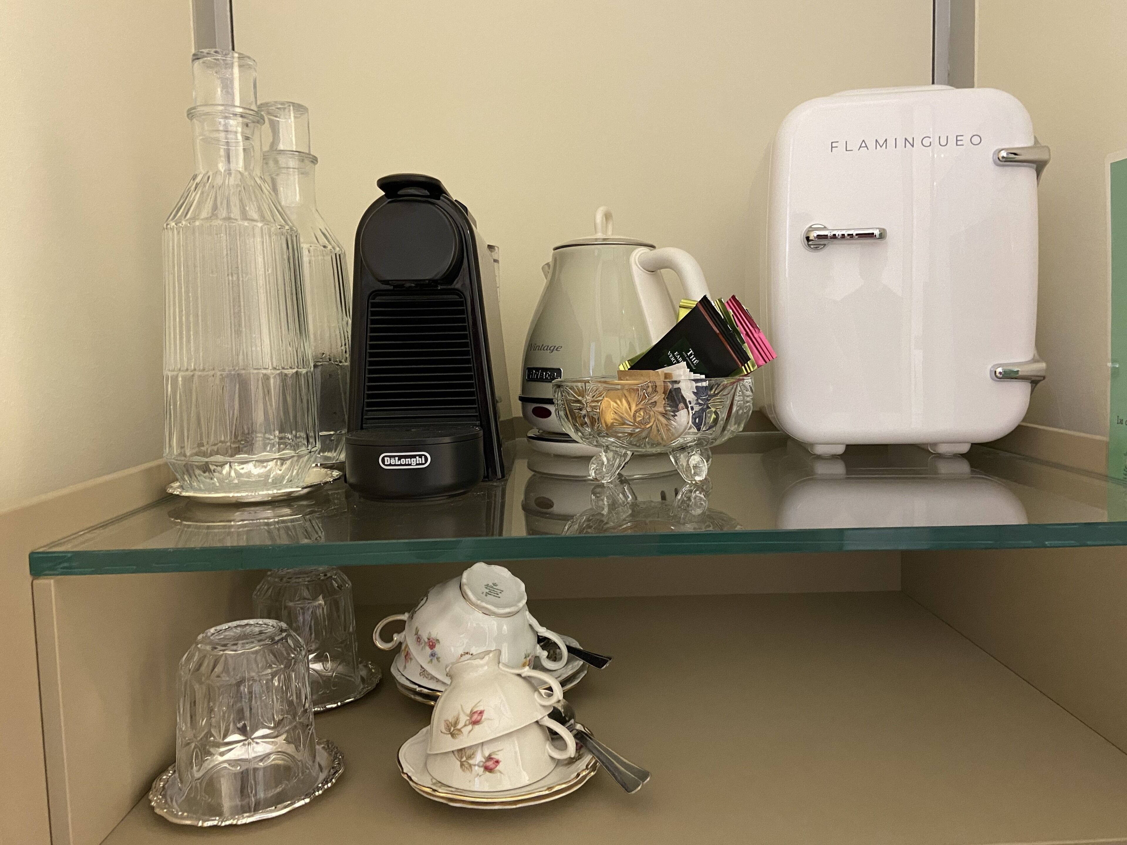 Une étagère en verre sur laquelle sont posés une machine à café, une théière et un vieux réfrigérateur.