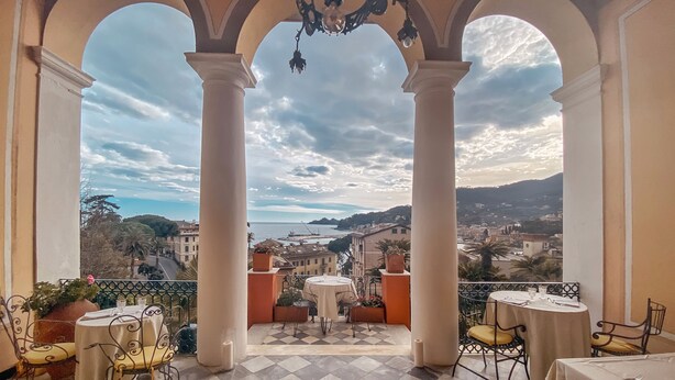 A terrace with a checkered floor, white columns, and tables with chairs.