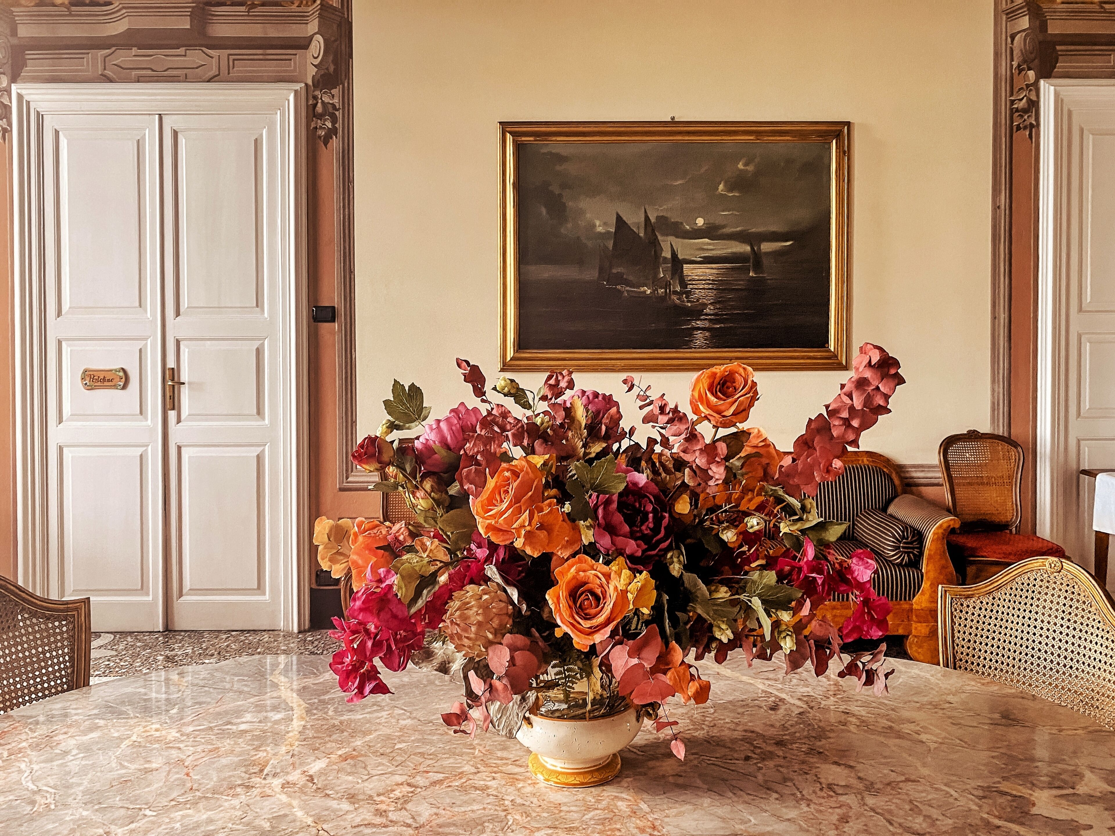 A room with a marble table, a floral arrangement, a framed painting, and a door with a sign.