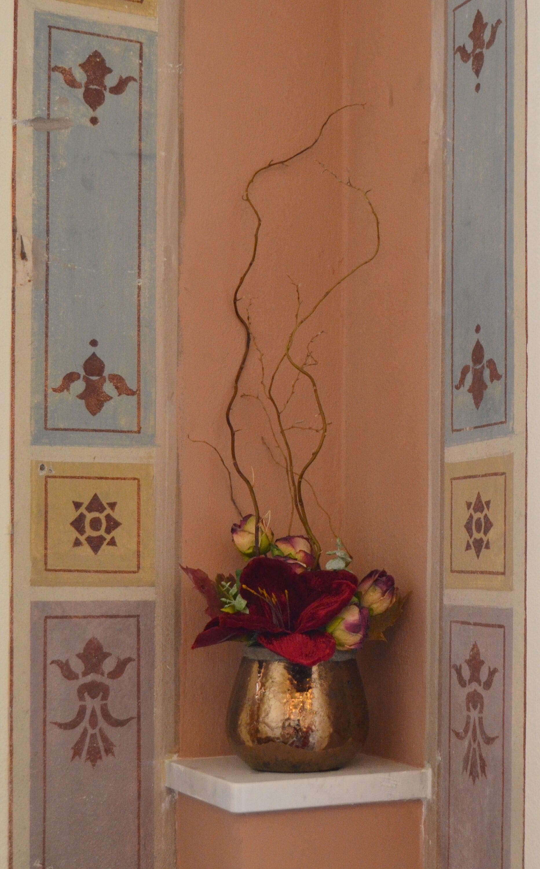 A wall with decorative panels and a small shelf holding a vase with flowers.