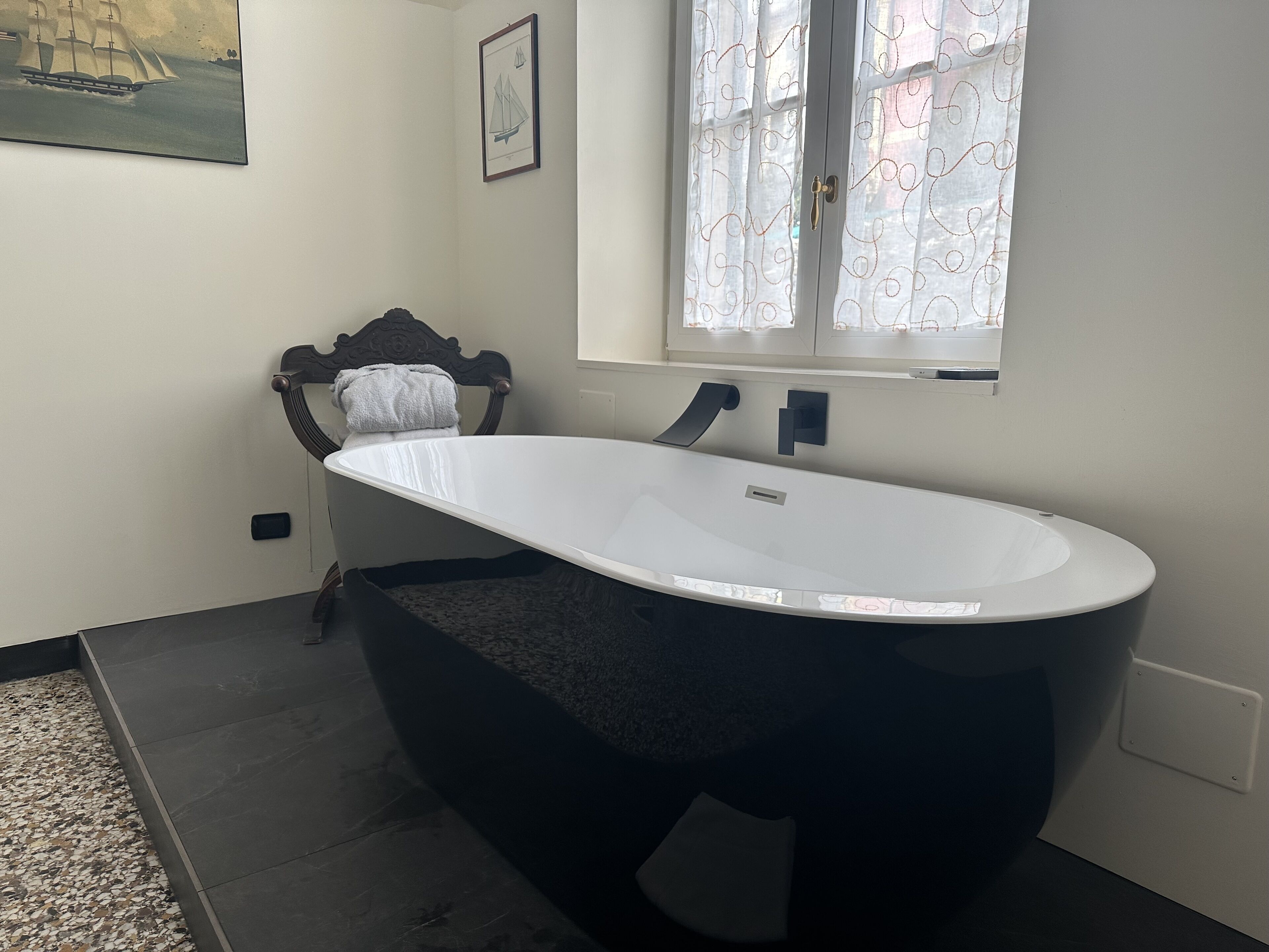 Une salle de bain avec une baignoire sur pieds, un porte-serviettes, une fenêtre avec des rideaux et un tableau au mur.