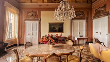 Ein Esszimmer mit Marmortisch, goldenen Stühlen, einer Chandelierleuchtre und einer floralen Tischdekoration.
