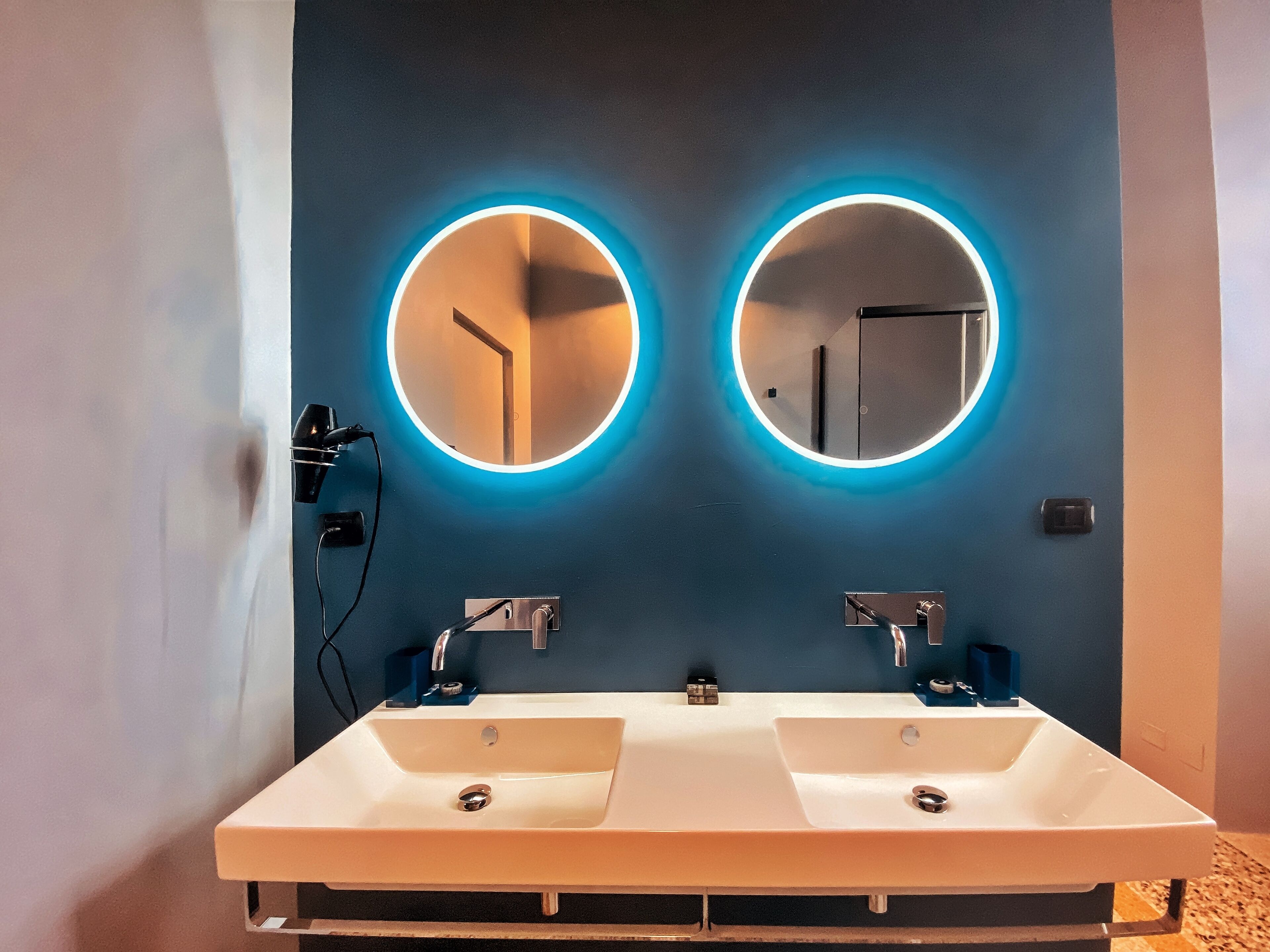 Ein modernes Badezimmer mit zwei Waschbecken, jeweils mit Spiegel und einer runden Beleuchtung.