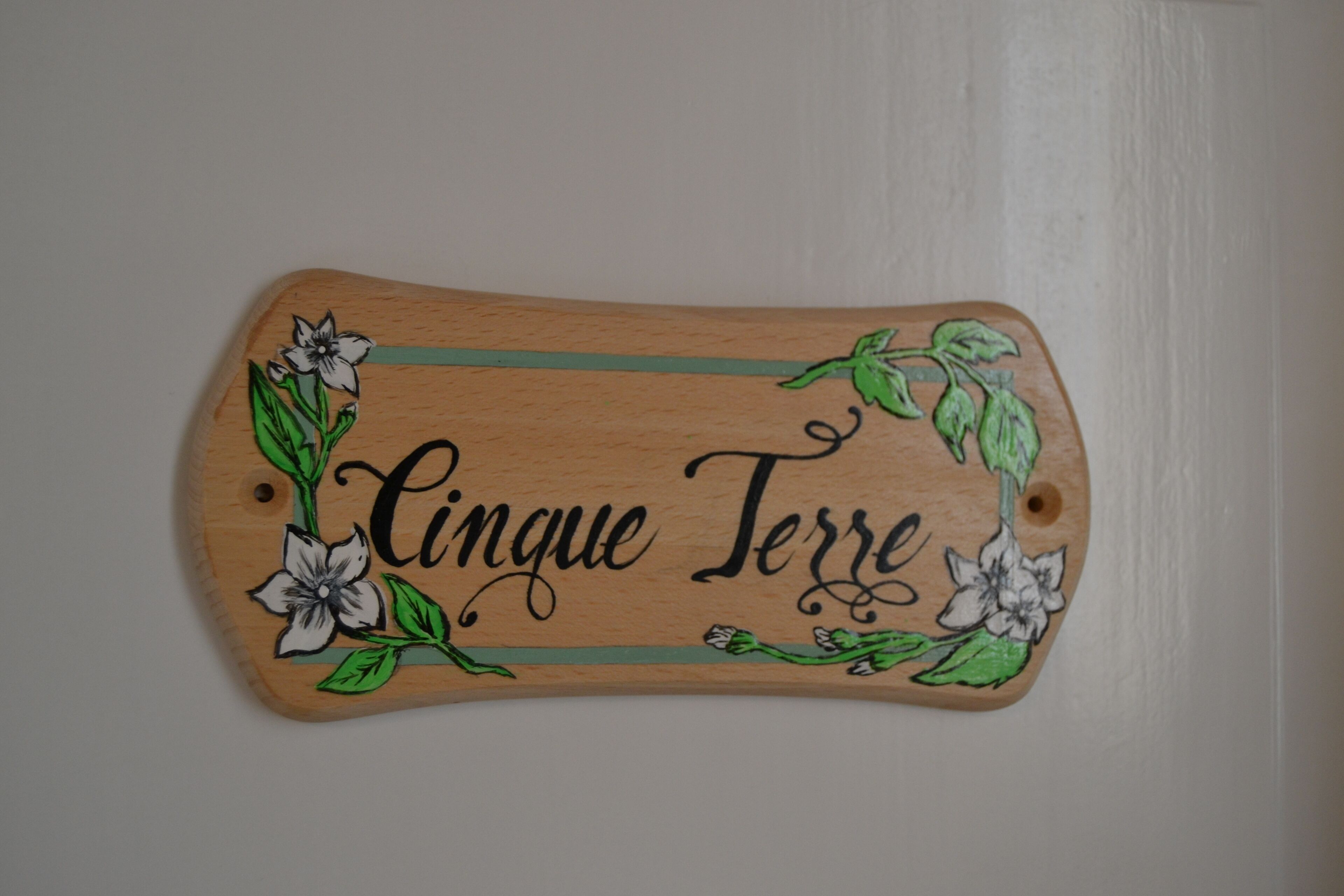 Un letrero de madera con el texto 'Cingue Terre' rodeado de motivos florales.