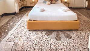 A hotel room with a large bed, a decorative ceiling, a painting, and a door.