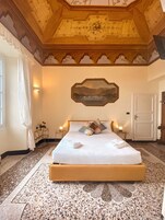 Una camera d'albergo con un letto grande, un soffitto decorato, un quadro e una porta.