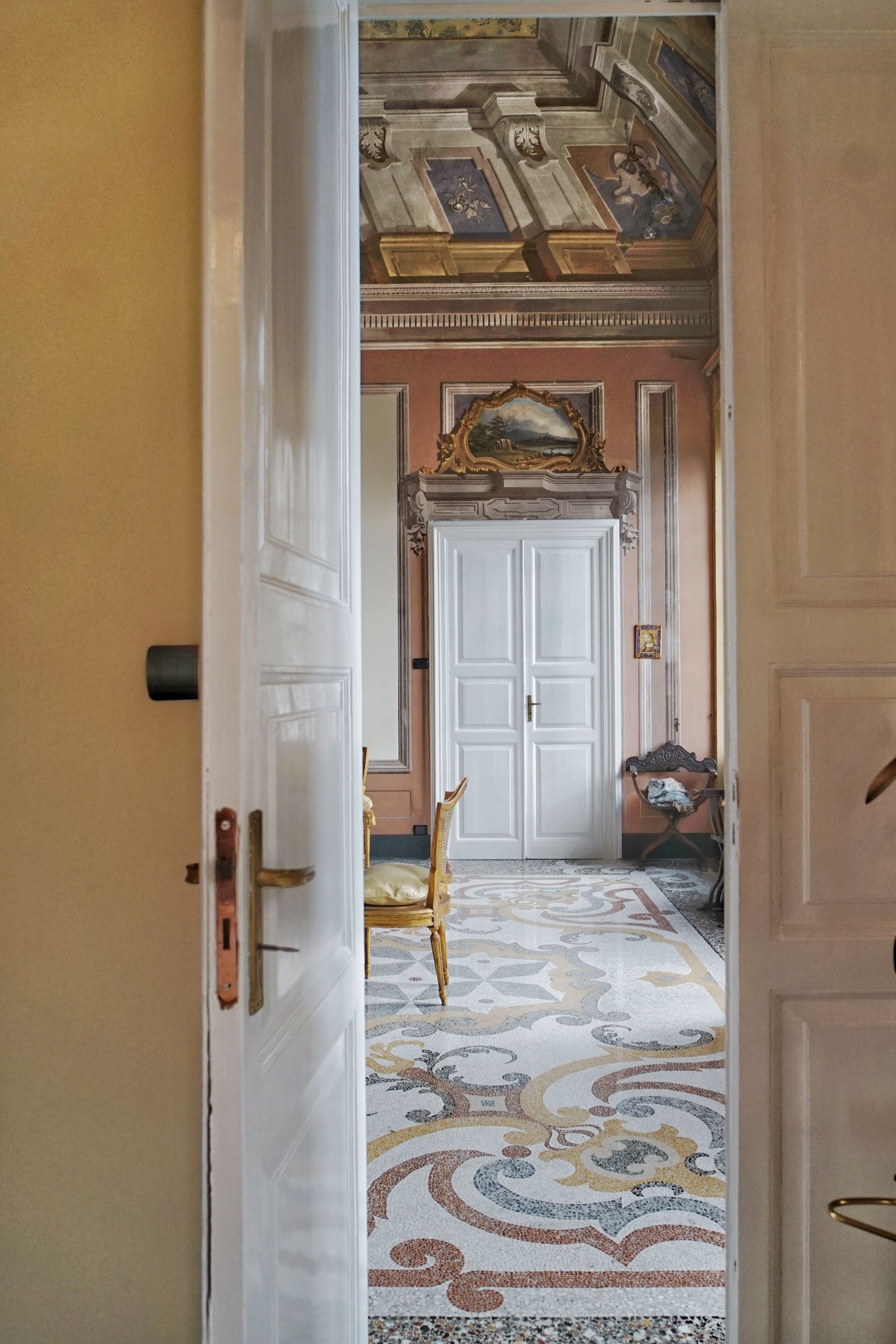 An interior hallway with a patterned floor, a white door, and a framed painting above it.