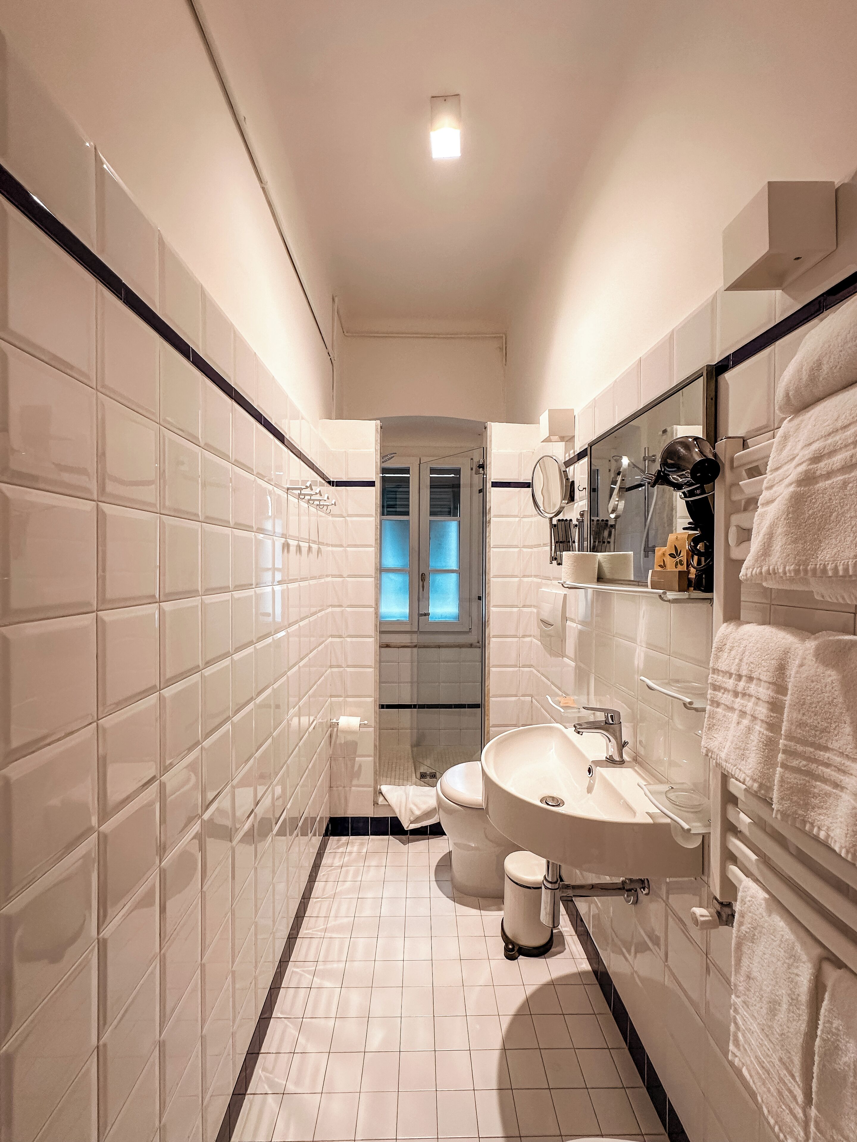 Une salle de bain moderne avec des carreaux blancs, des toilettes, un lavabo et un miroir.