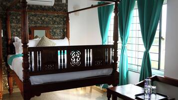 A four-poster bed with a wooden frame and a canopy, a small wooden table with glasses, and a window with curtains.