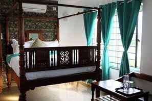A four-poster bed with a wooden frame and a canopy, a small wooden table with glasses, and a window with curtains. - Le Holiday Inn (Vanur)