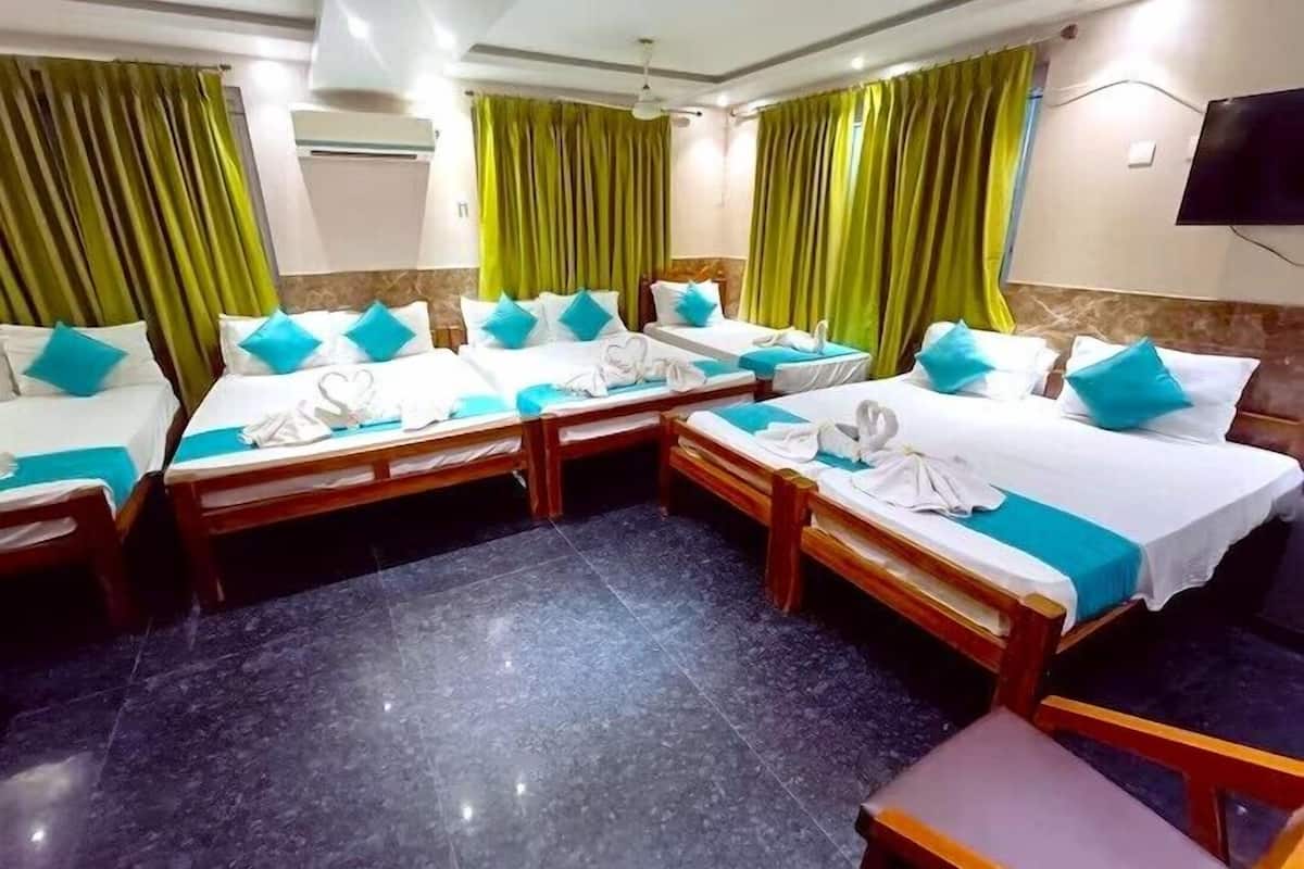 Une chambre d’hôtel avec quatre lits disposés en forme de U, des rideaux verts, un téléviseur à écran plat et un sol en marbre.