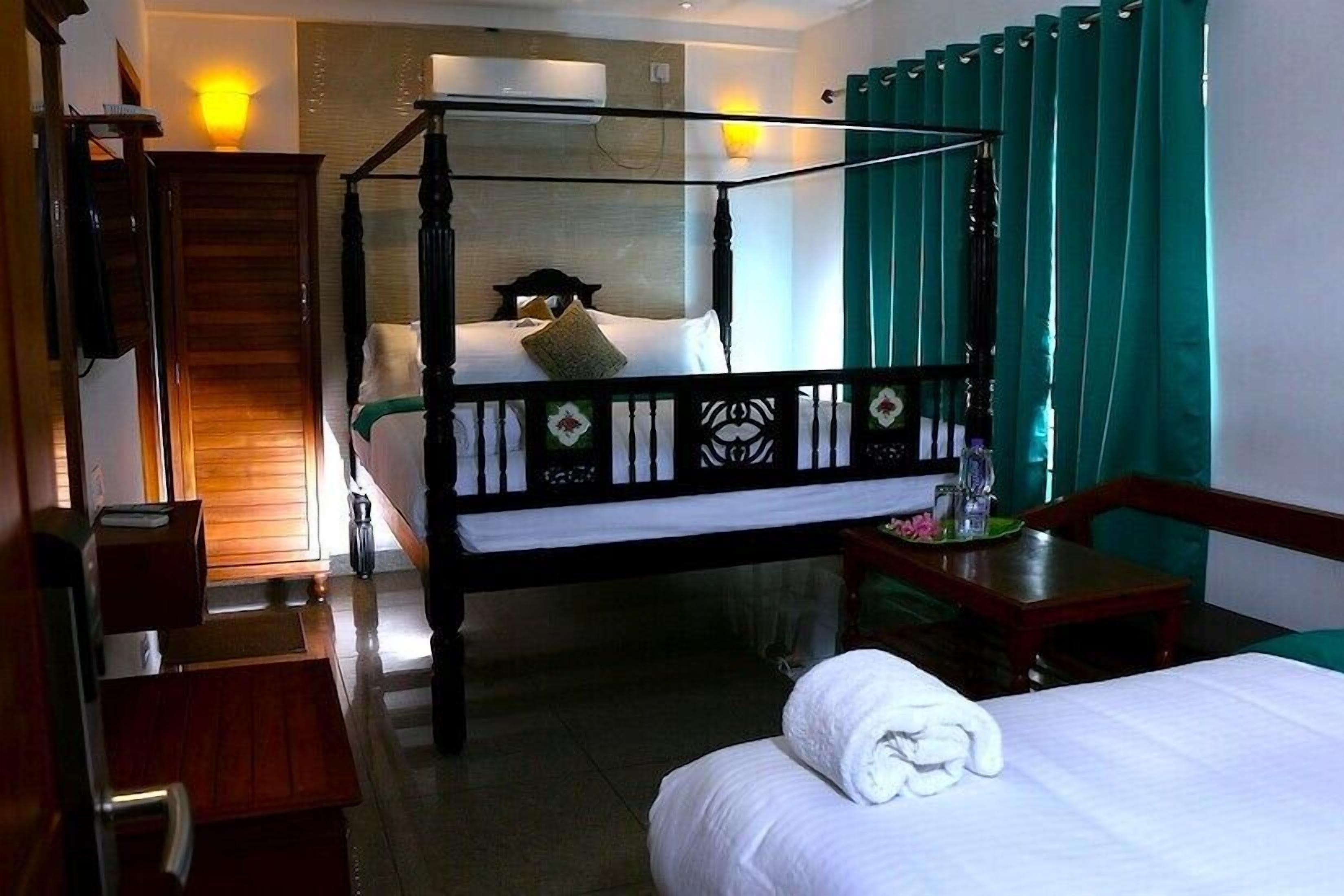 A hotel room with a four-poster bed, a wooden desk, a chair, a small table with a lamp, and a staircase leading to another room.