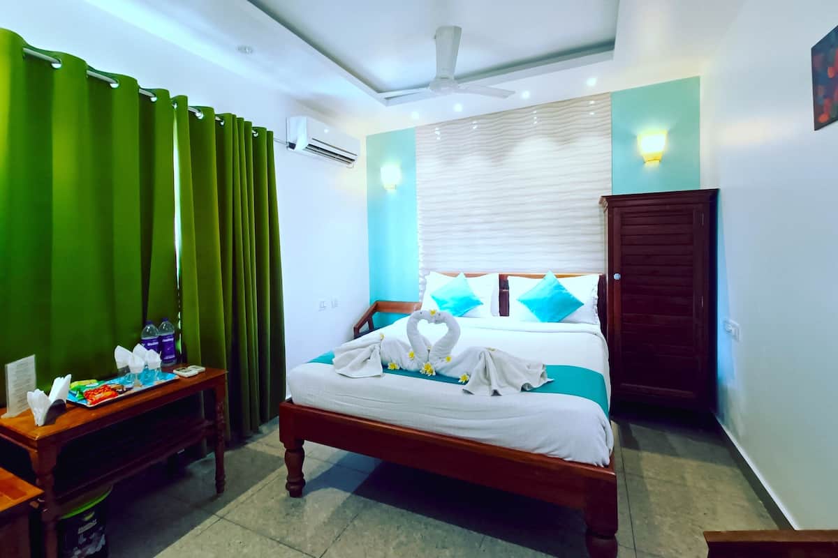 Une chambre d’hôtel avec un lit, une table de chevet, une armoire en bois, un rideau vert et un ventilateur de plafond.