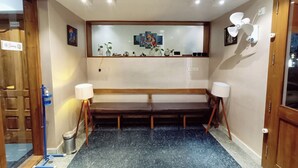 Zona de recepció d'hotel amb una banca, un safataire i un mirall fixat a la paret.