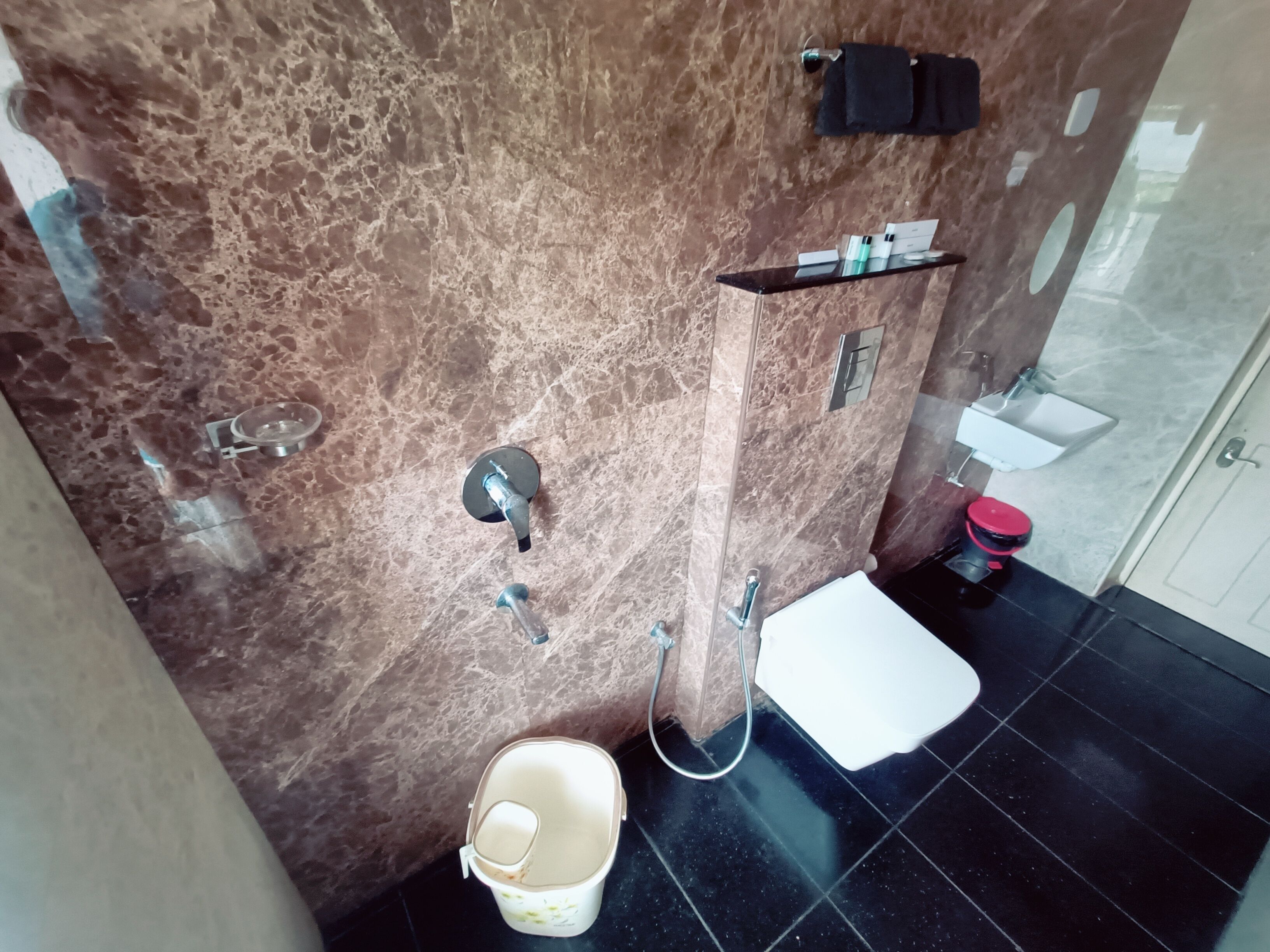 A bathroom with a marble wall, a white sink, a toilet, and a shower area.