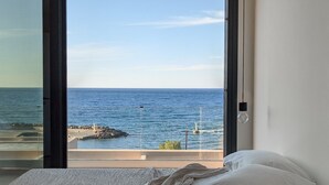 Ein Schlafzimmer mit großem Fenster und Meerblick, ein Bett mit weißer Bettwäsche sowie Ausblick auf die zerklüftete Küste.