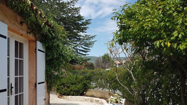 A narrow stone pathway leading to a white door with shutters, surrounded by lush greenery and a view of the sea. - Petit Fleur Studio with Terrace (Ampus)