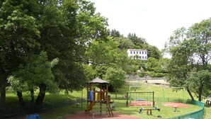 A playground with a wooden climbing structure, swings, and a slide, surrounded by a green fence and trees. - Petit Fleur Studio with Terrace (Ampus)