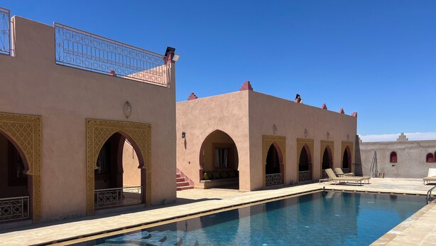 Un espace piscine avec une eau d’un bleu limpide, situé à côté d’un bâtiment doté d’arcades et d’un balcon.