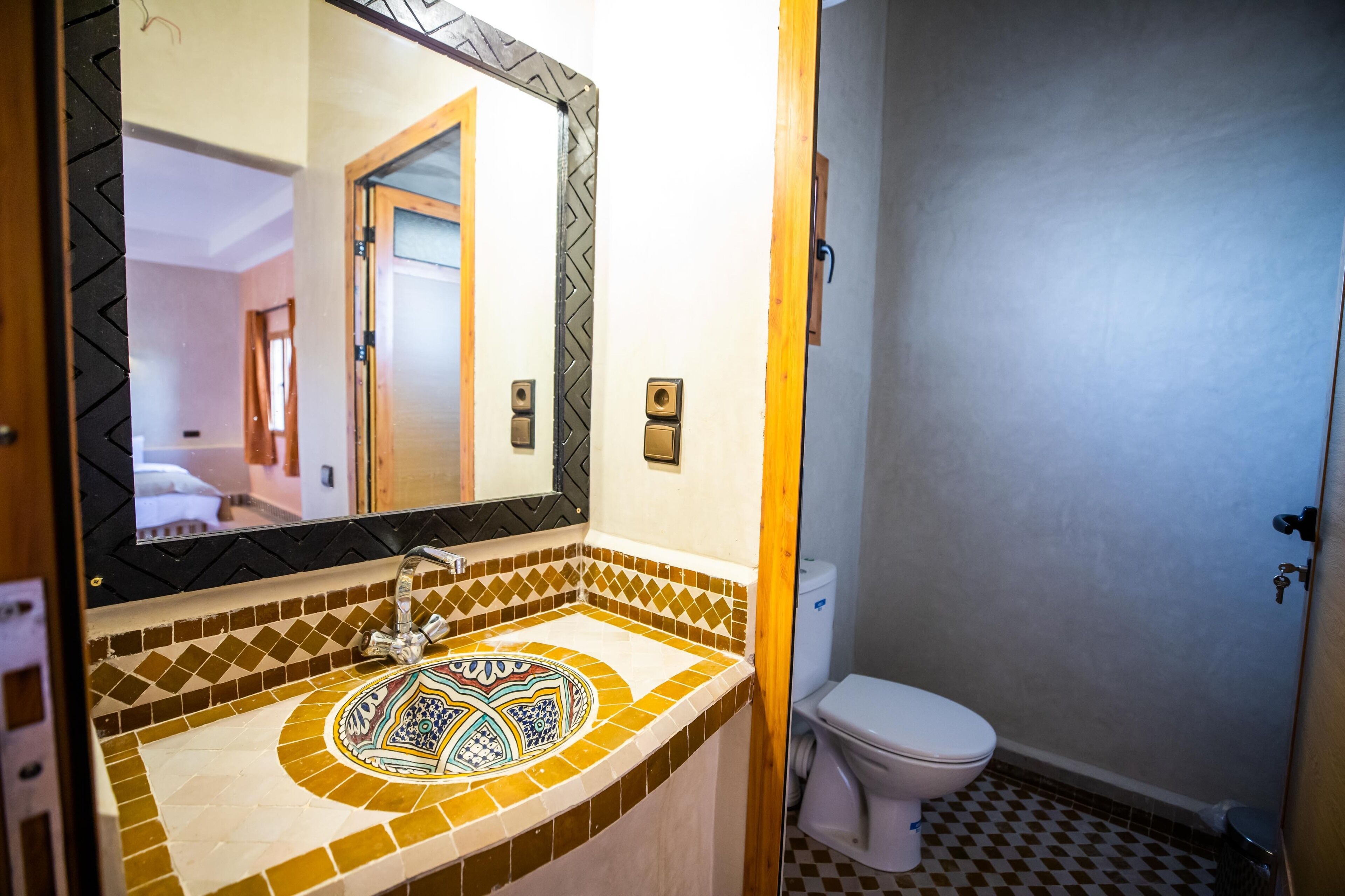 Une salle de bain avec un lavabo carrelé, un miroir et des toilettes.