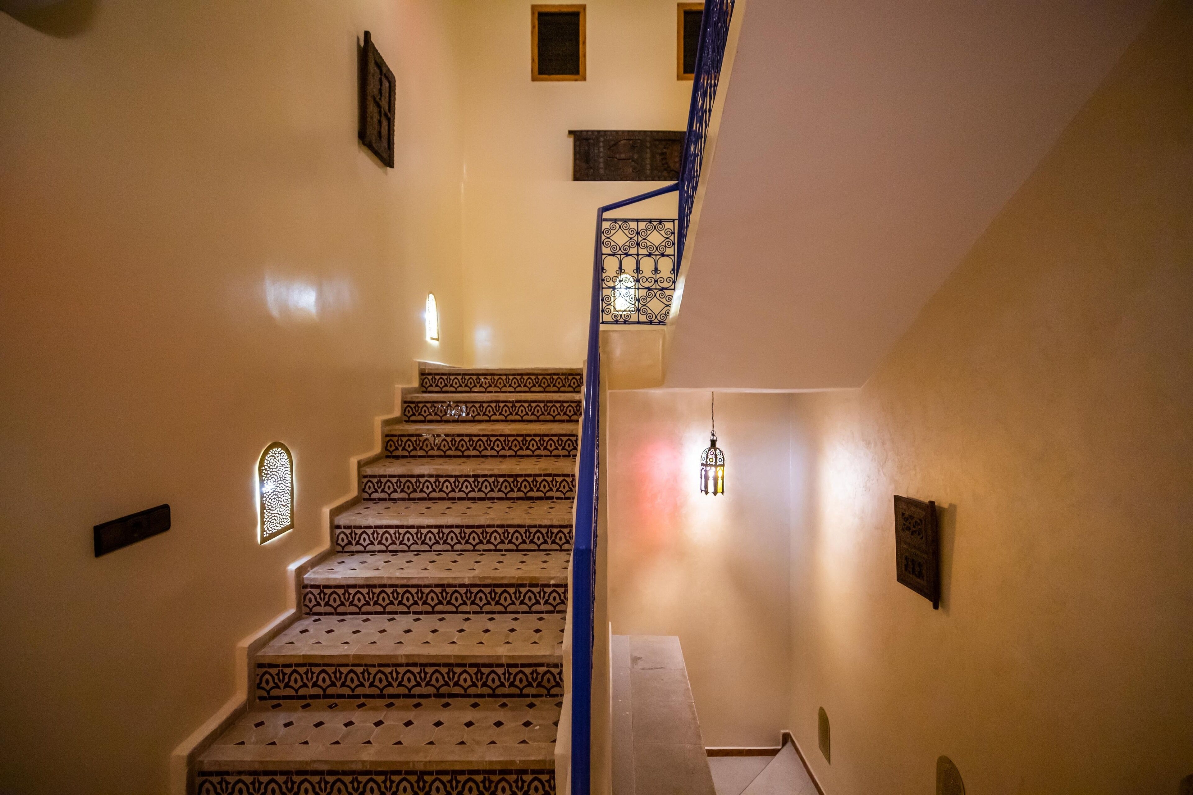 A staircase with patterned steps and a blue railing, leading to a landing with a wall-mounted light fixture.