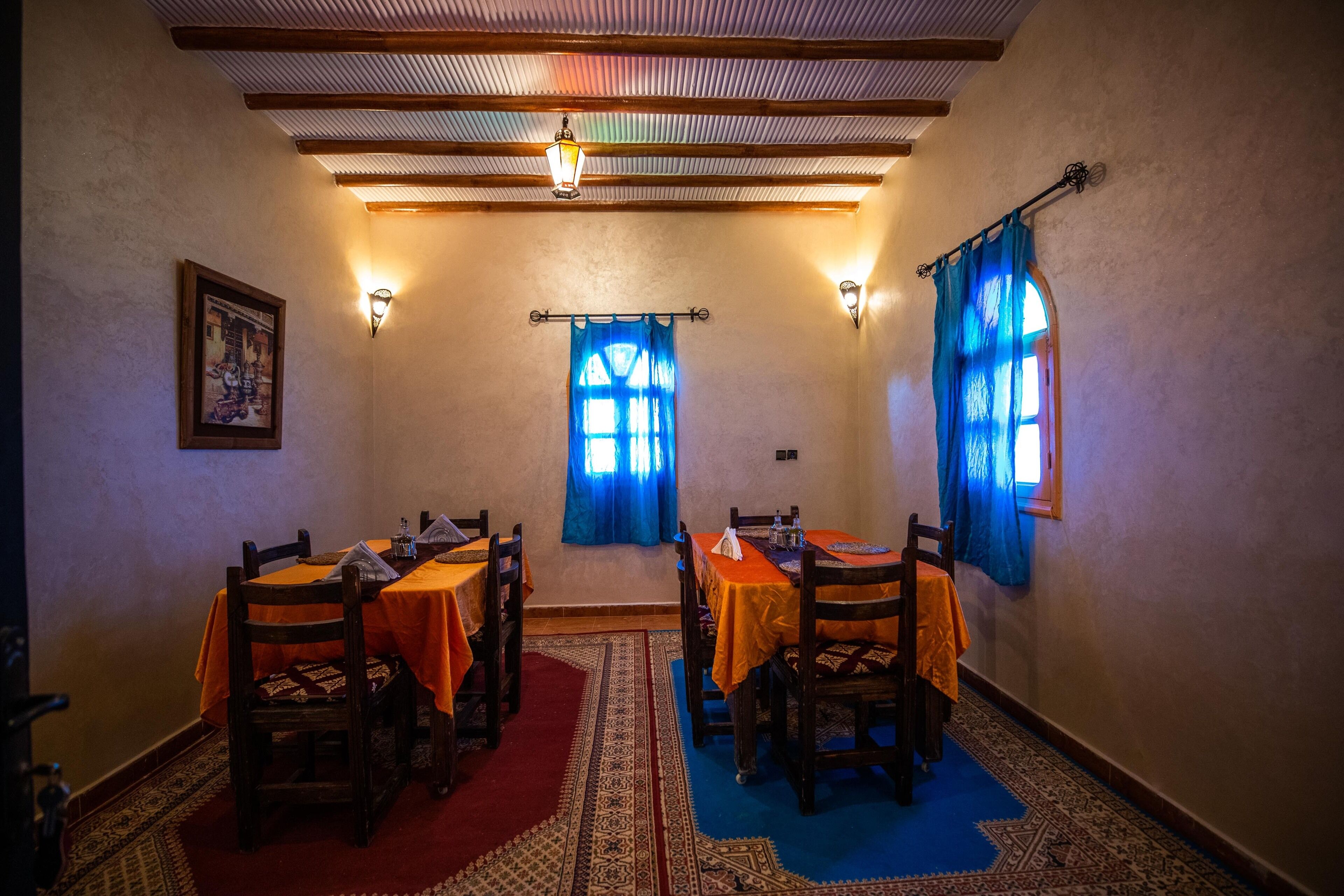 A dining area with wooden tables and chairs, blue curtains, and patterned rugs.