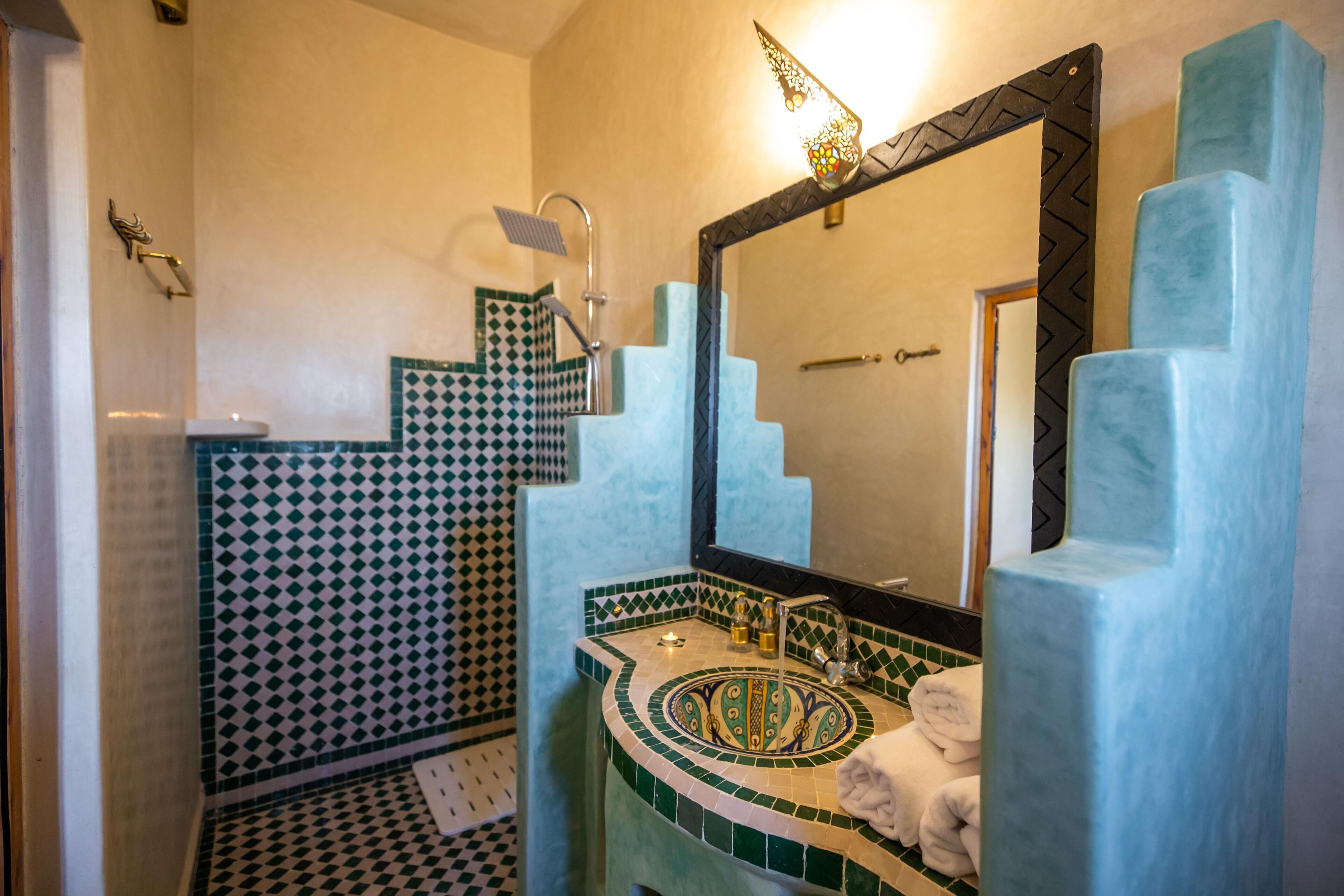Un baño con piso de baldosas, un lavamanos con lavabo decorativo, un espejo con marco geométrico y una zona de ducha.