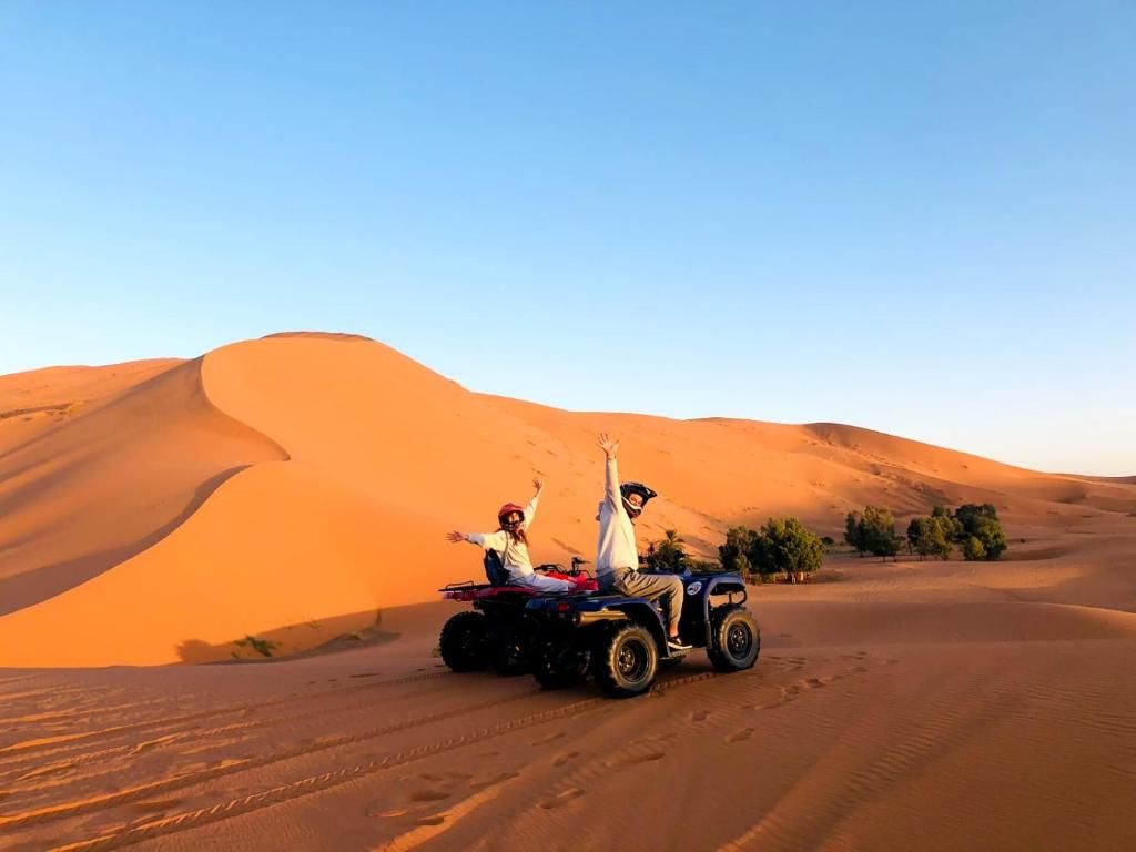 Two people on an ATV in a desert with sand dunes.