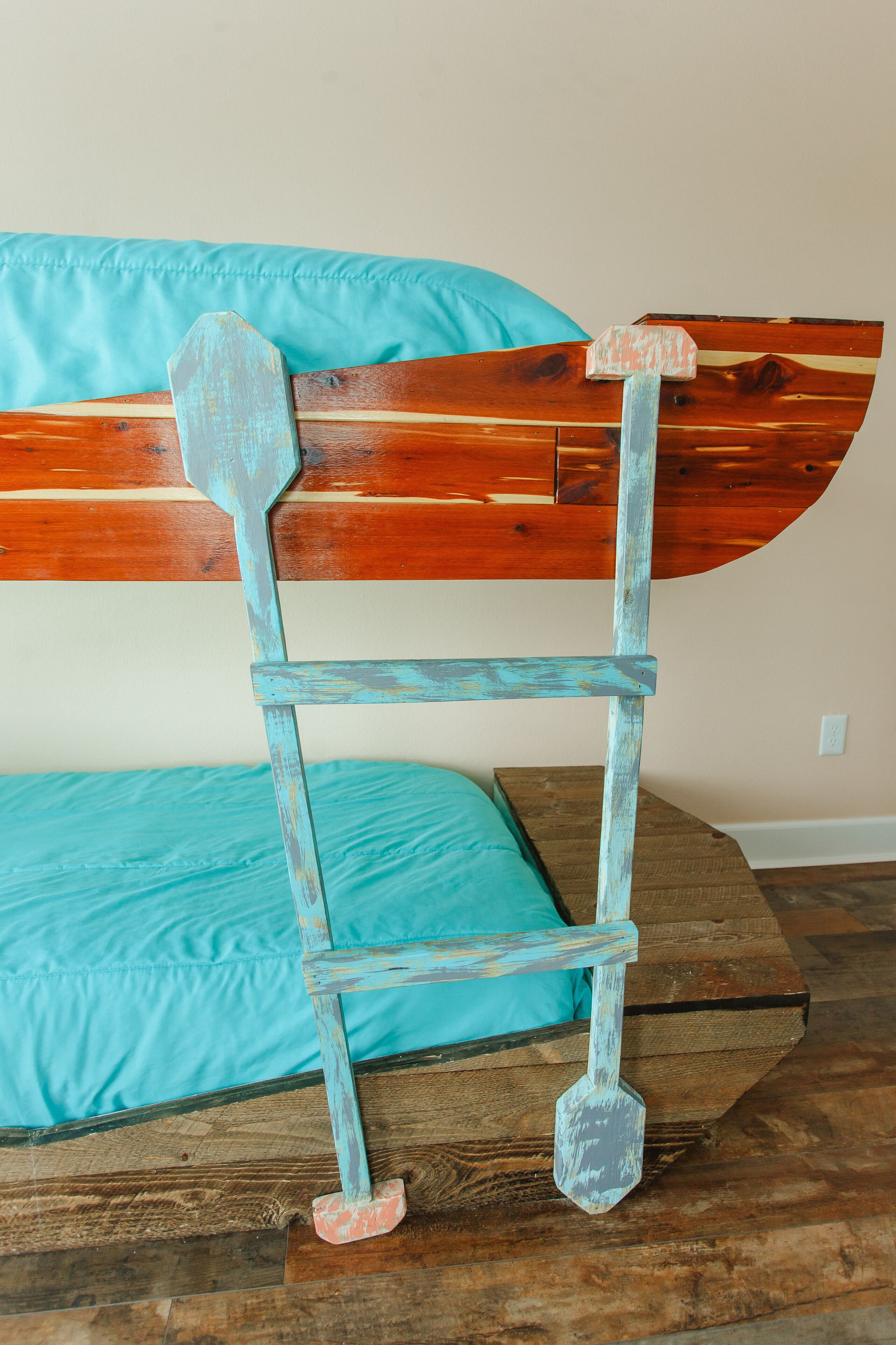 A rustic wooden bed frame with a turquoise mattress and matching pillow.