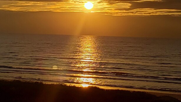 Solnedgang over et roligt hav, hvor solen reflekteres i vandet.