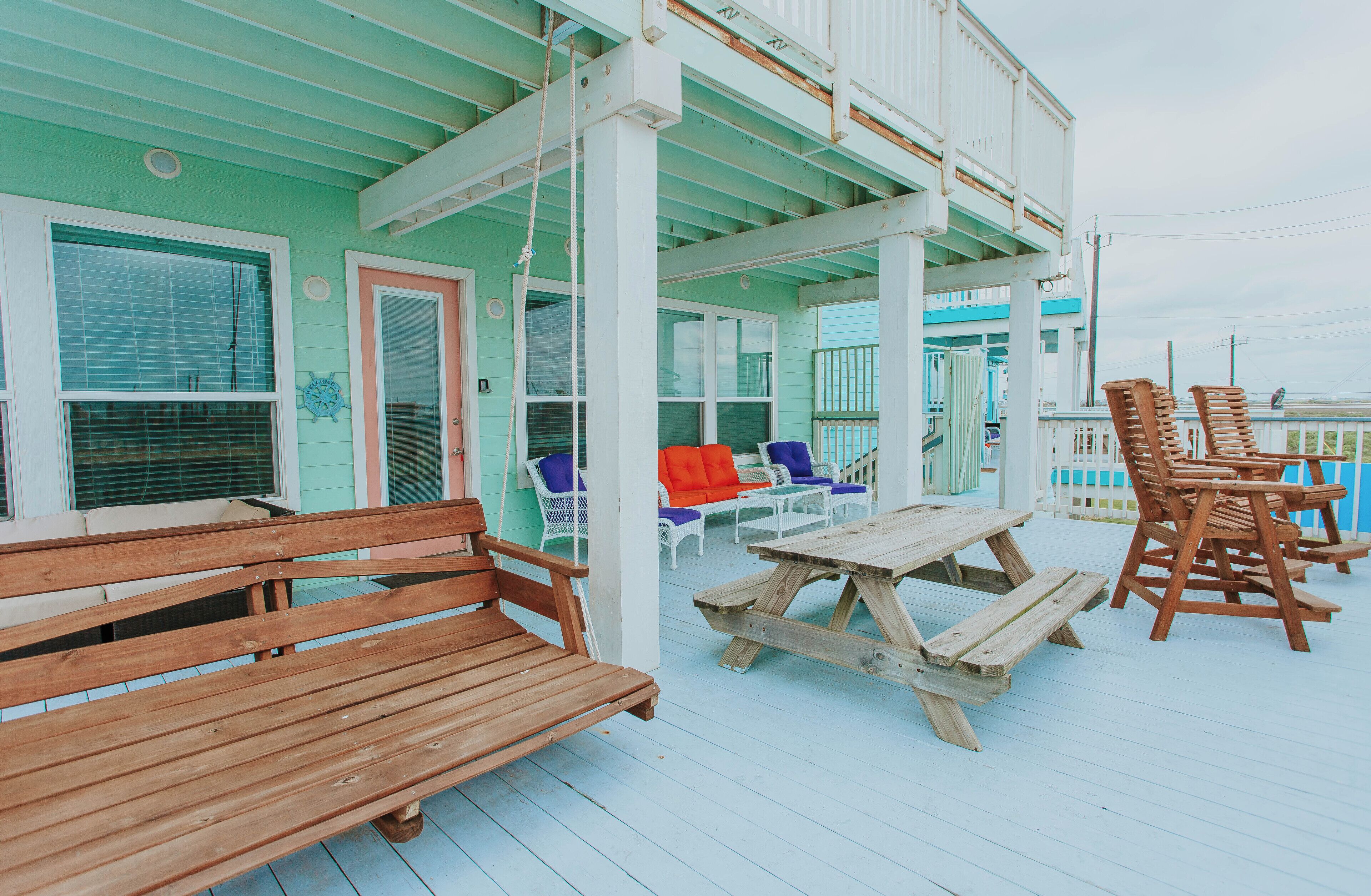 A wooden deck with benches, a table, and colorful chairs.