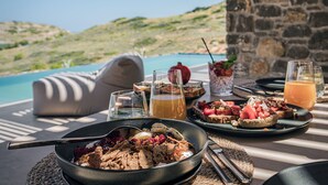 Una mesa de comedor con alimentos para el desayuno, un tazón de cereal y una vista a una piscina y colinas al fondo.