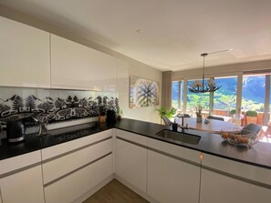 Una cocina moderna con armarios blancos, una encimera negra y vistas a un comedor con una mesa y sillas.