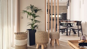 Ein modernes Wohnzimmer mit einer großen Topfpflanze, gewebten Poufs und einem Essbereich mit Tisch und Stühlen.