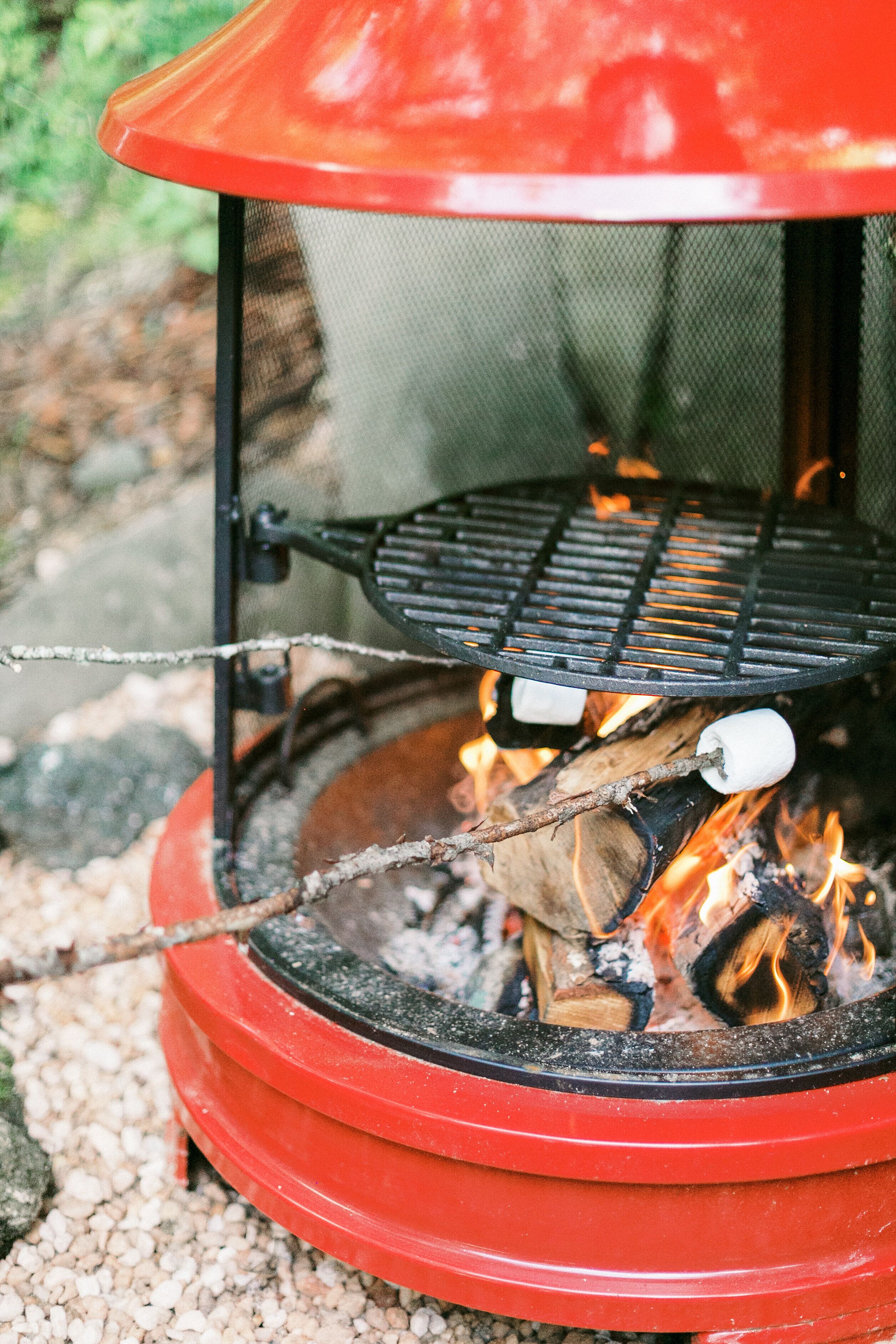Ein tragbarer Grill für den Außenbereich mit roter Abdeckung und einem Drahtgitter, auf einem Kiesgrund platziert.