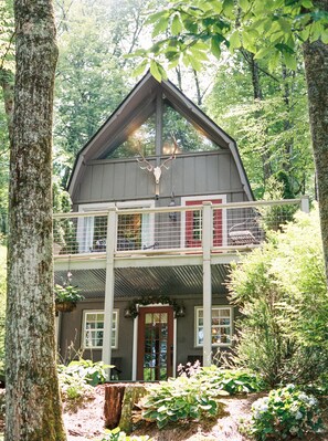 Experience the tranquility of the forest from the balcony overlooking the treetops, with a traditional gabled roof and central entrance.